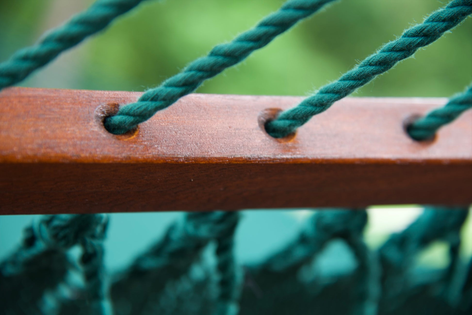 Polyester cords threaded through the drilled hardwood spreader bar of a green Island Oasis hammock