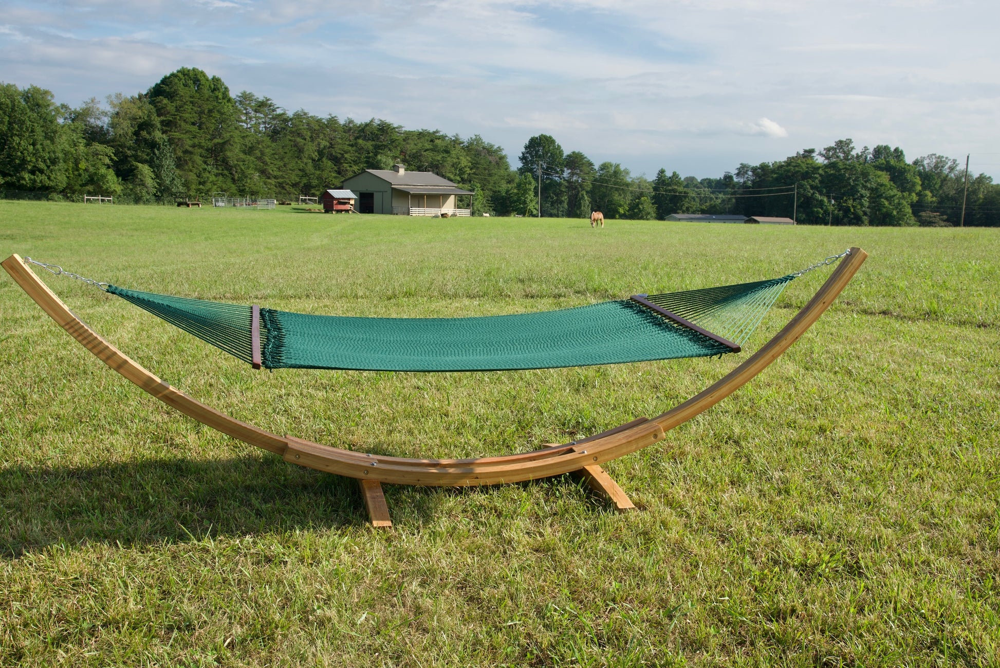 Green Island Oasis hammock hanging on the Wood Arc Hammock Stand in a pasture with a barn behind