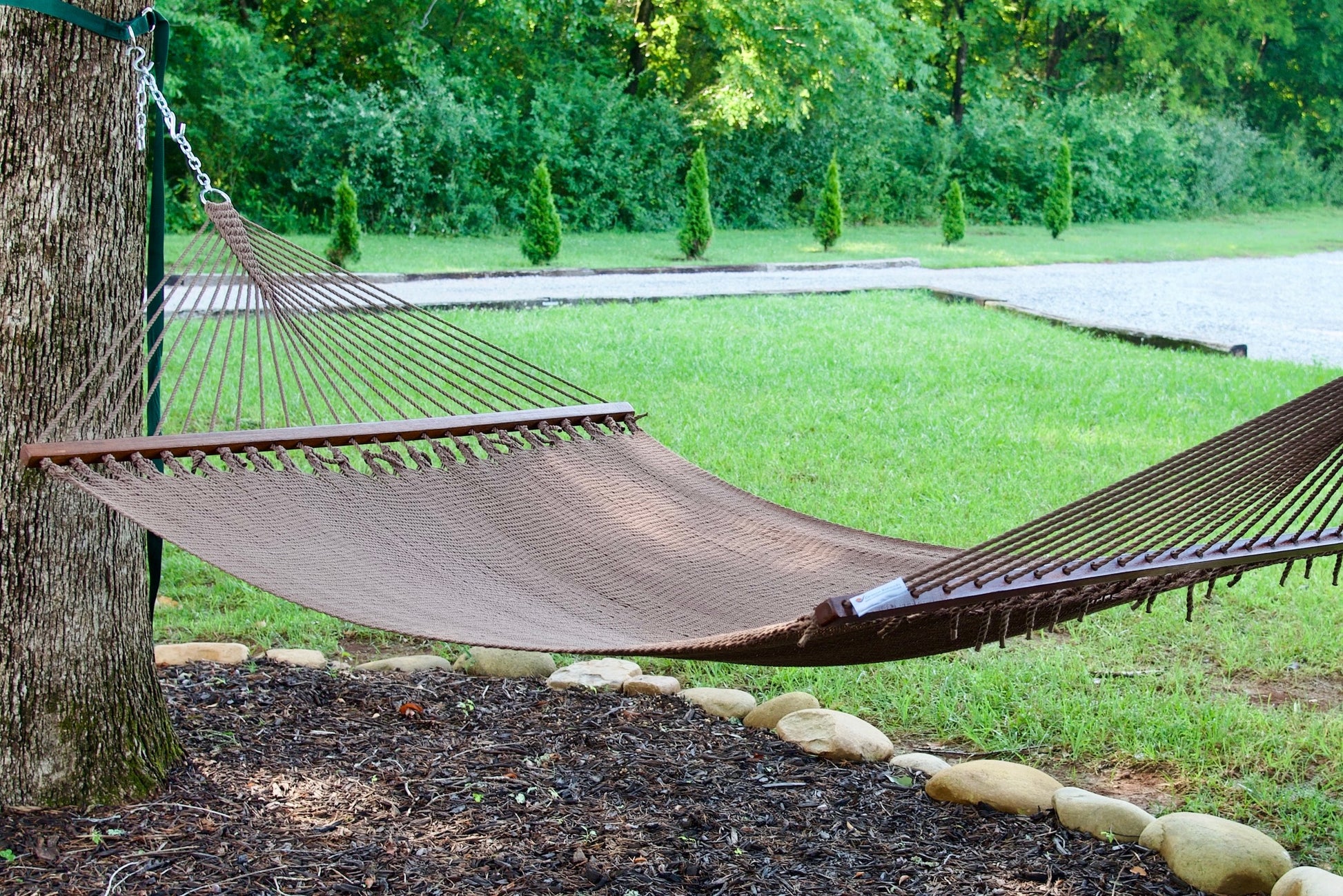 Mocha Island Oasis hammock hung between a tree and a post in a green backyard with a gravel path behind