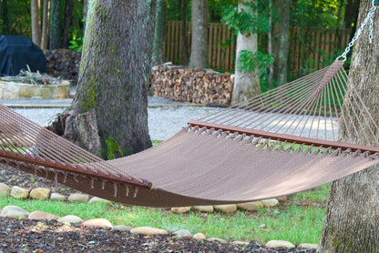 Mocha Island Oasis hammock hung between two trees beside a fire pit and stacked firewood