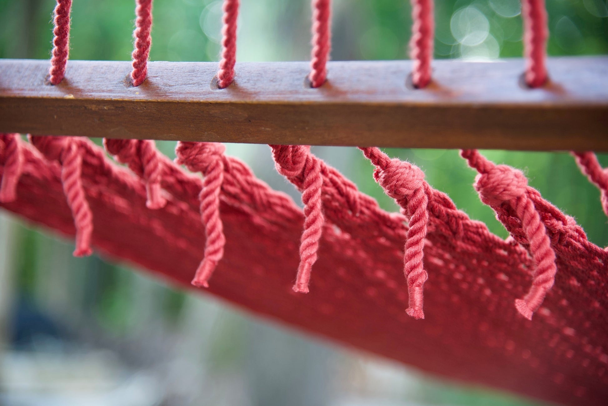 Polyester cords threaded through the drilled hardwood spreader bar of a red Island Oasis hammock
