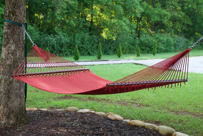 Red Island Oasis hammock hung between a tree and a post in a green backyard with a gravel path behind