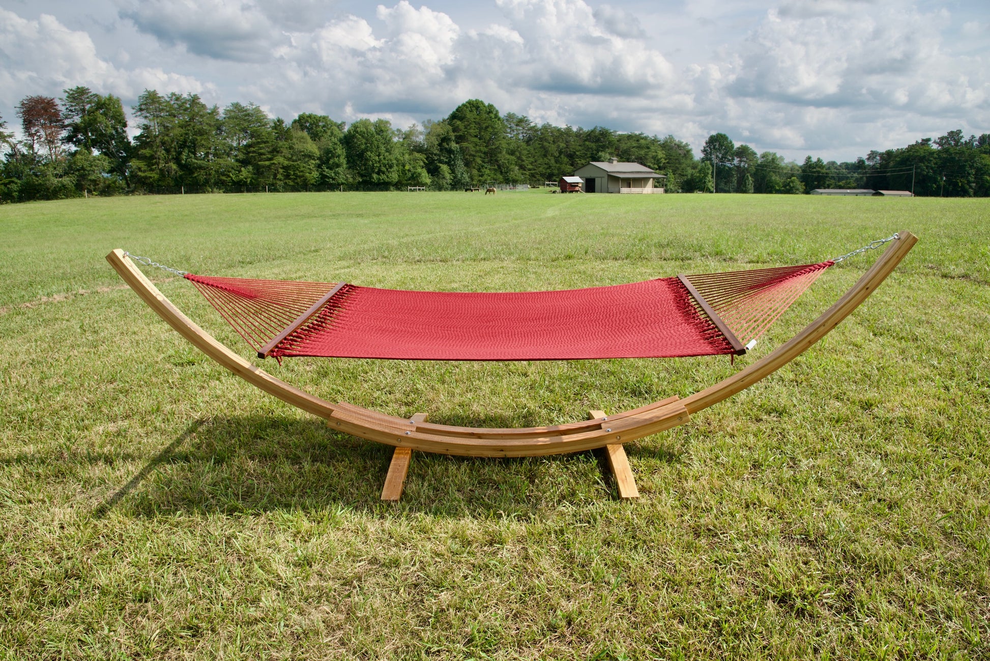 Red Island Oasis hammock hanging on the Wood Arc Hammock Stand in a pasture with a barn behind