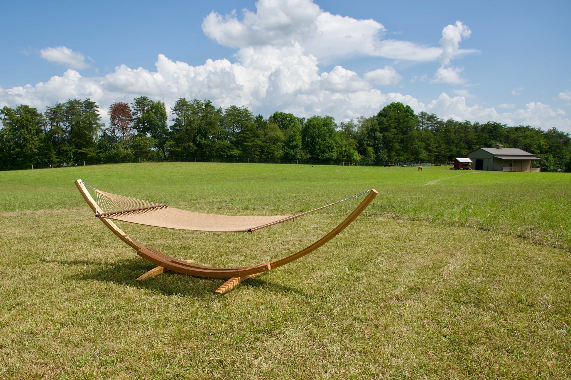 Tan Island Oasis hammock hanging on the Wood Arc Hammock Stand in a pasture with a barn behind