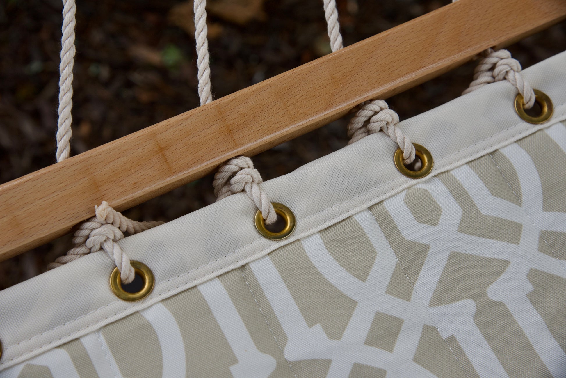 Brass roll-rimmed grommets and knotted polyester end cords along the wood spreader bar of a beige pattern Island Tranquility hammock