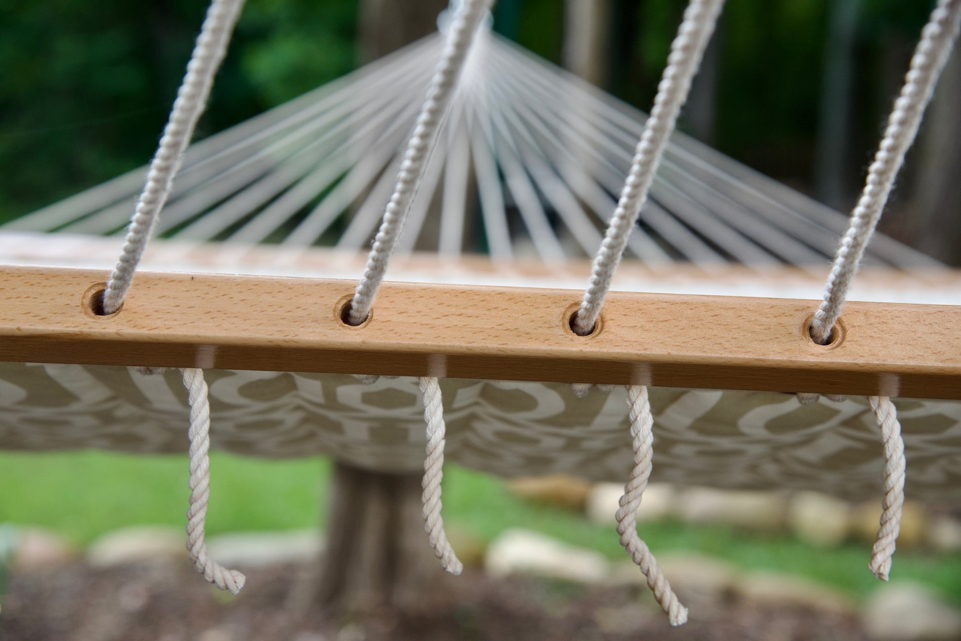 Polyester end cords threaded through the drilled wood spreader bar of a beige pattern Island Tranquility hammock