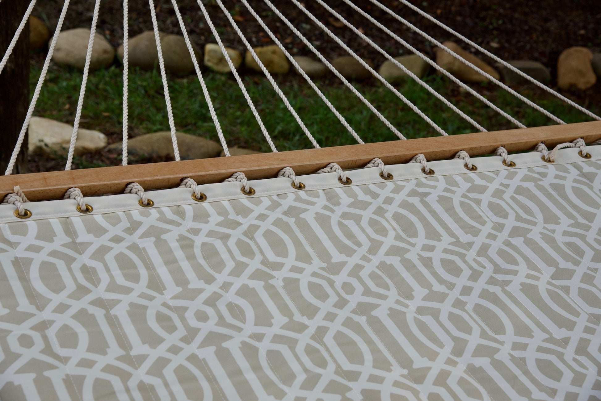 Polyester end cords fanning from the wood spreader bar of a beige pattern Island Tranquility hammock