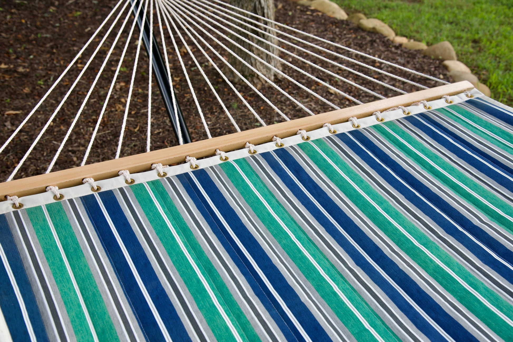Polyester end cords fanning from the wood spreader bar of a green and blue stripe Island Tranquility hammock
