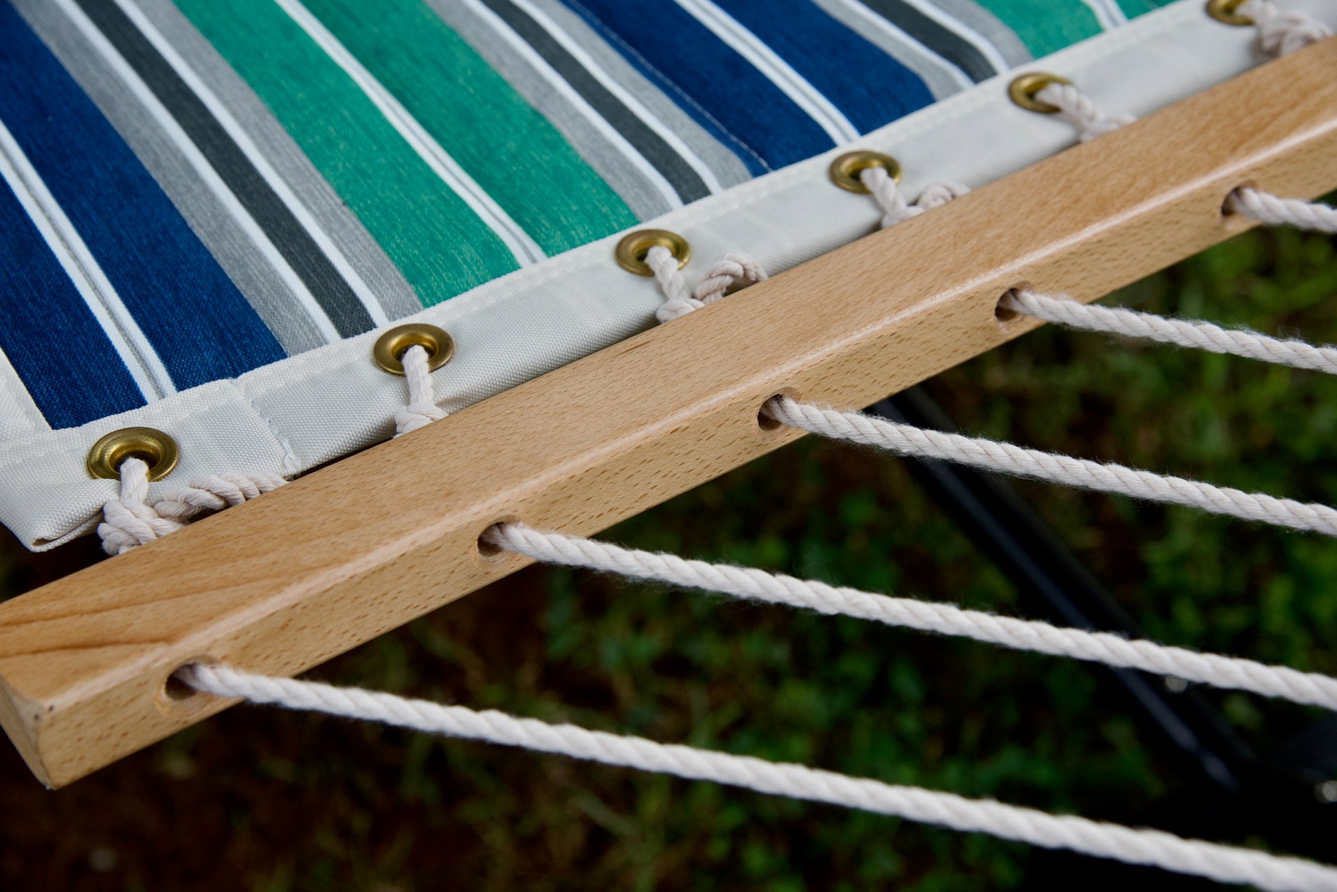 Polyester end cords threaded through the drilled wood spreader bar of a green and blue stripe Island Tranquility hammock