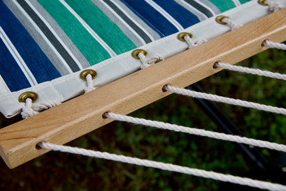 Polyester end cords threaded through the drilled wood spreader bar of a green and blue stripe Island Tranquility hammock