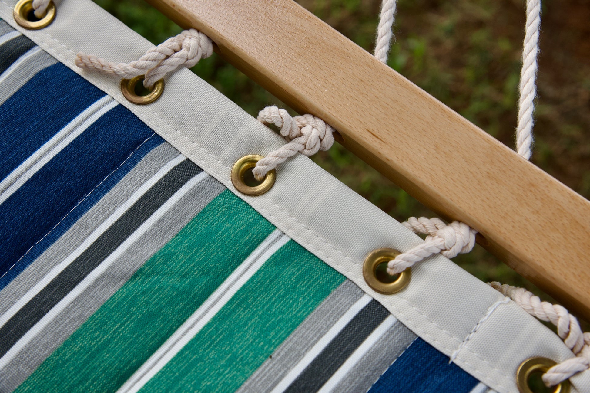 Brass roll-rimmed grommets and polyester end cords on the reinforced edge of a green and blue stripe Island Tranquility hammock