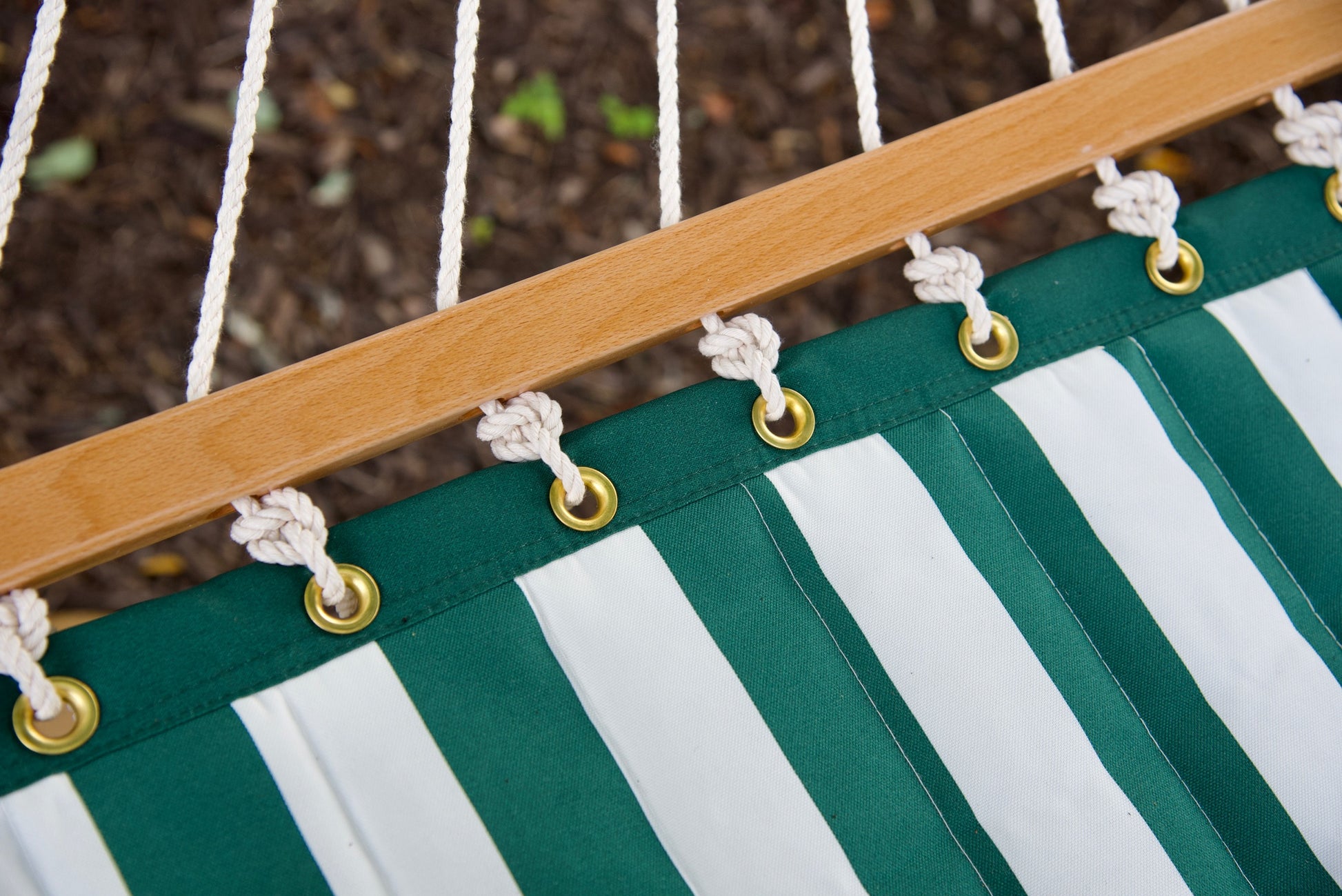 Brass roll-rimmed grommets and knotted polyester end cords along the wood spreader bar of a green stripe Island Tranquility hammock
