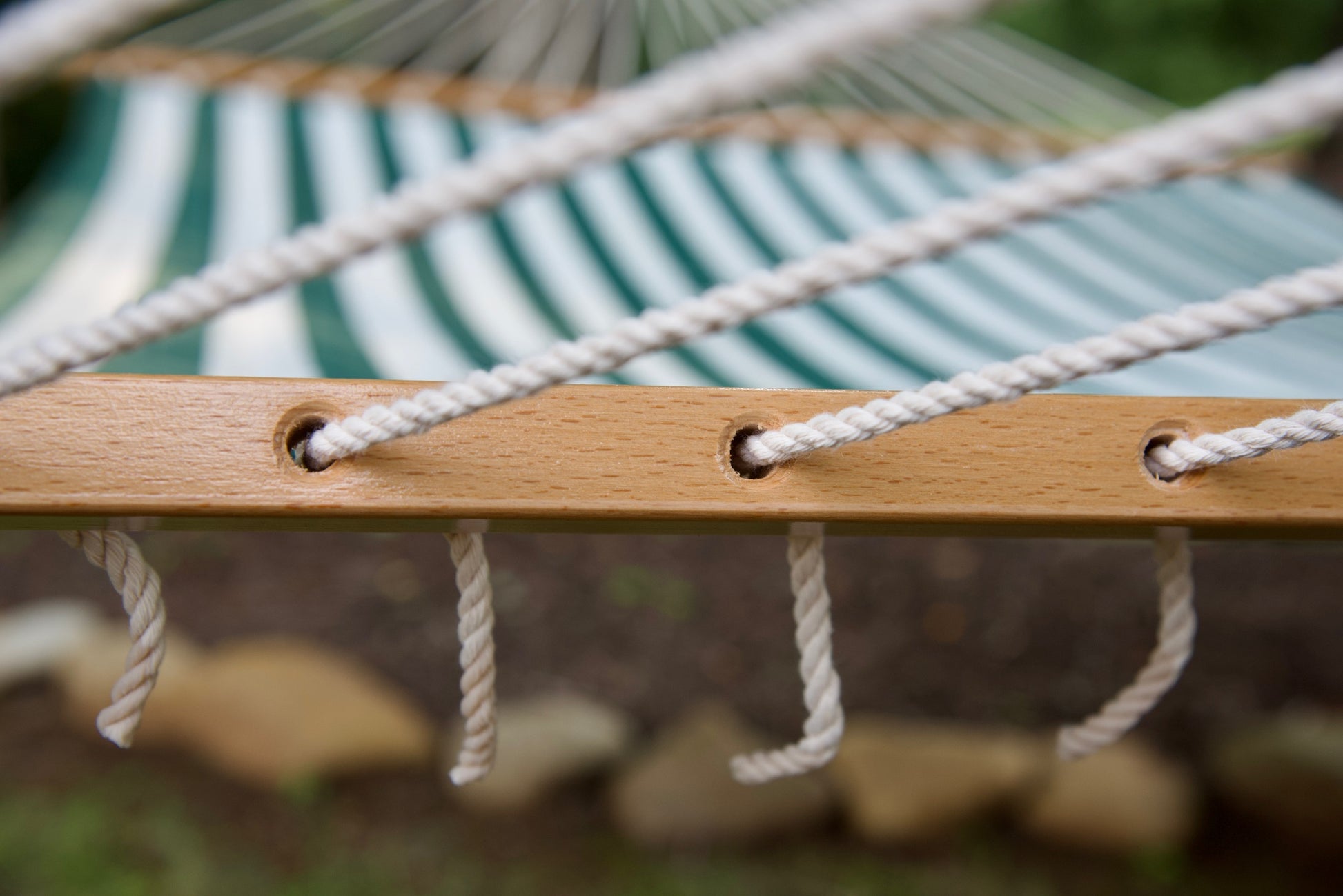 Polyester end cords threaded through the drilled wood spreader bar of a green stripe Island Tranquility hammock
