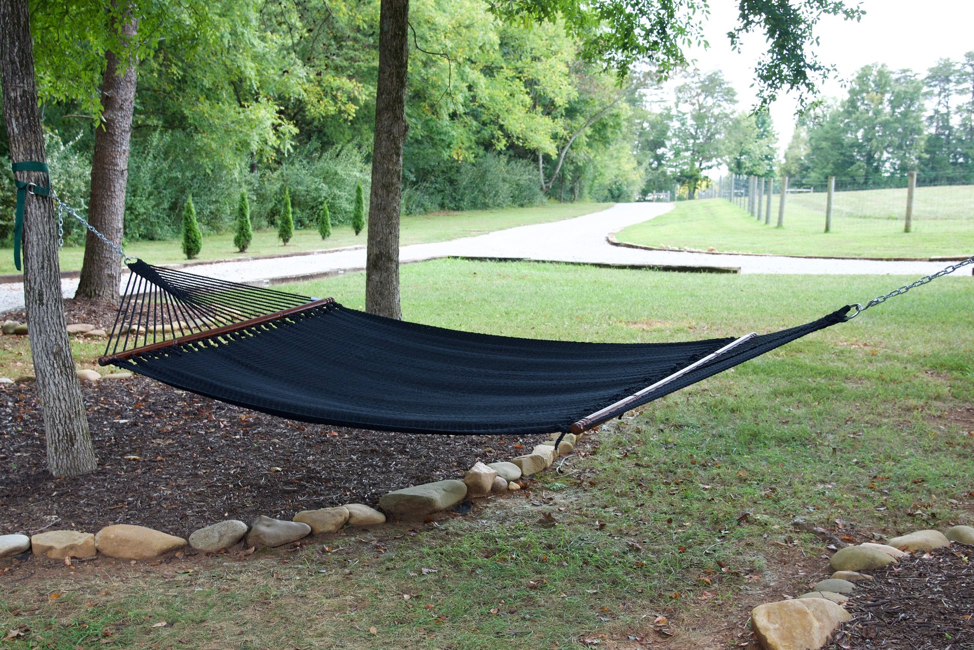 Black Jumbo Caribbean Hammock hanging between two trees in a backyard