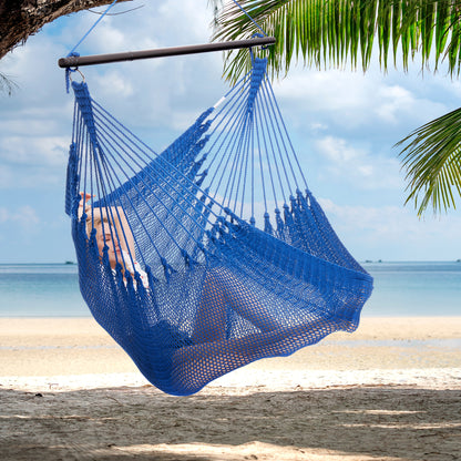 Person reclining in a dark blue Jumbo Caribbean Hammock Chair hung from a palm tree above a white sand beach