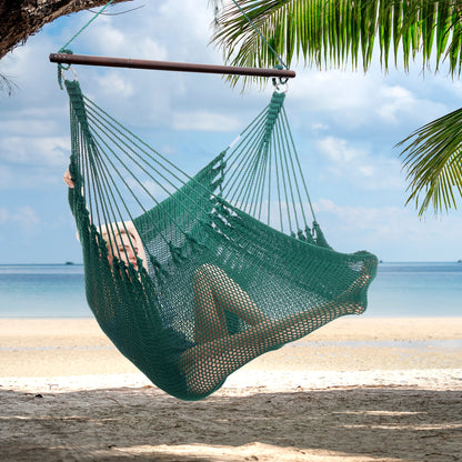 Person reclining in a green Jumbo Caribbean Hammock Chair hung from a palm tree above a white sand beach