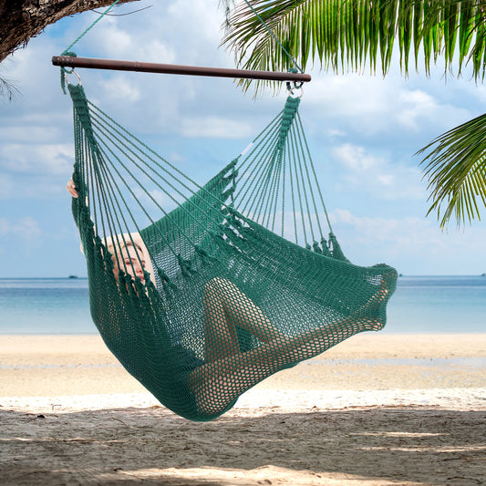 Person reclining in a green Jumbo Caribbean Hammock Chair hung from a palm tree above a white sand beach