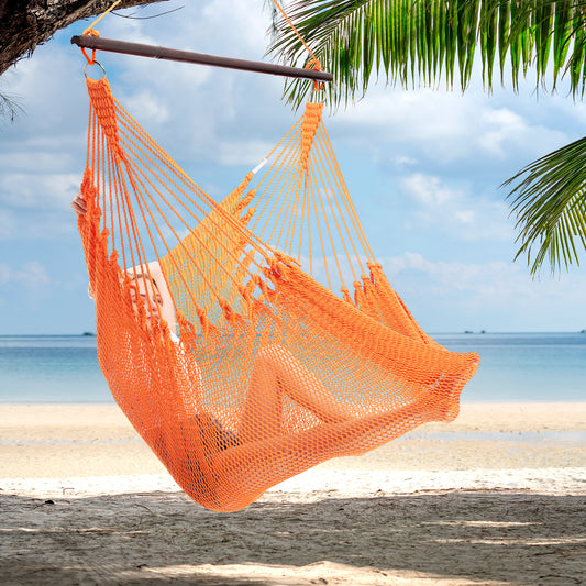 Person reclining in an orange Jumbo Caribbean Hammock Chair hung from a palm tree above a white sand beach