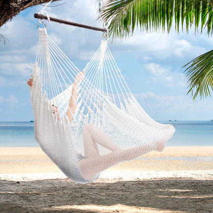 Person reclining in a white Jumbo Caribbean Hammock Chair hung from a palm tree above a white sand beach