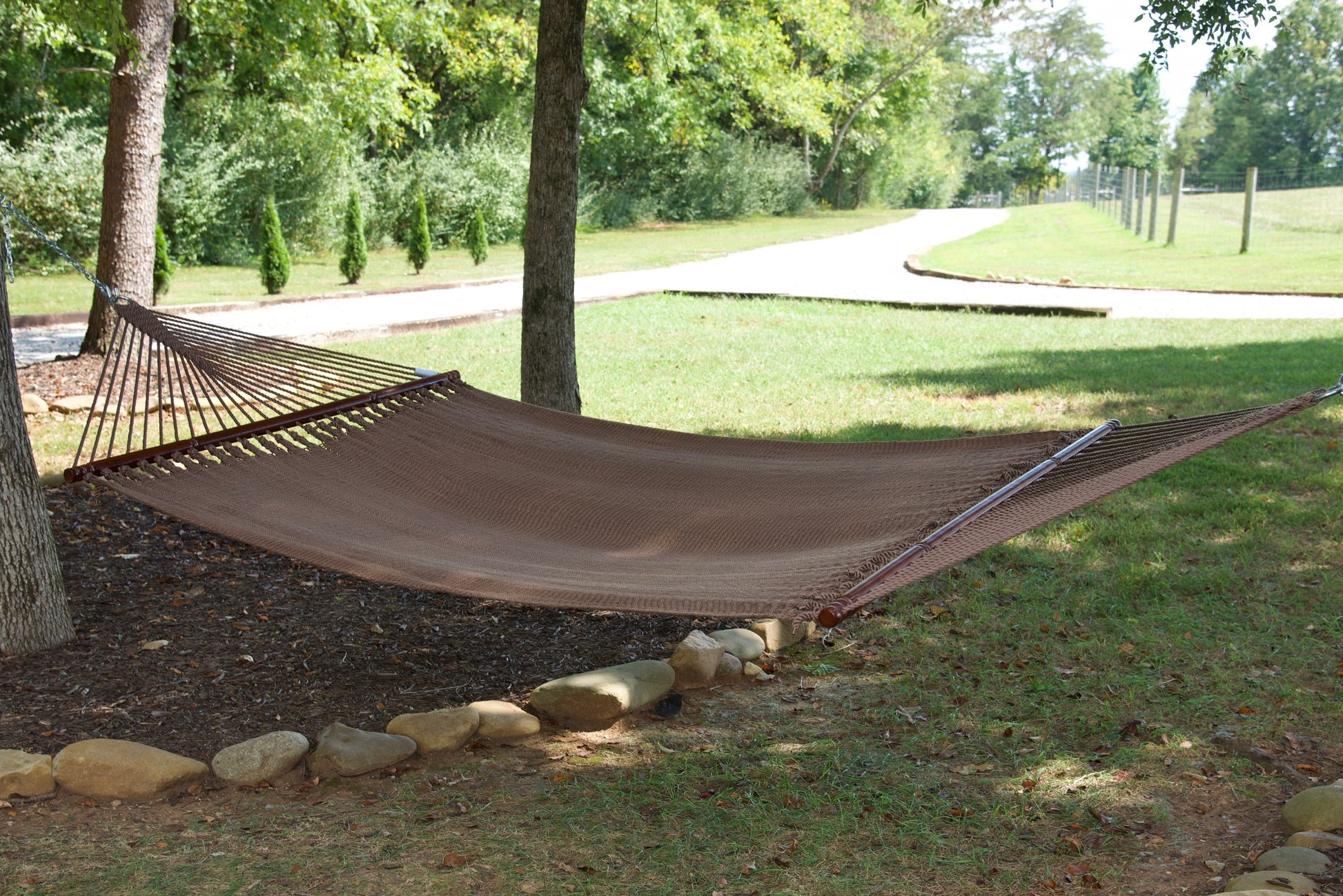 Mocha Jumbo Caribbean Hammock hanging between two trees in a backyard