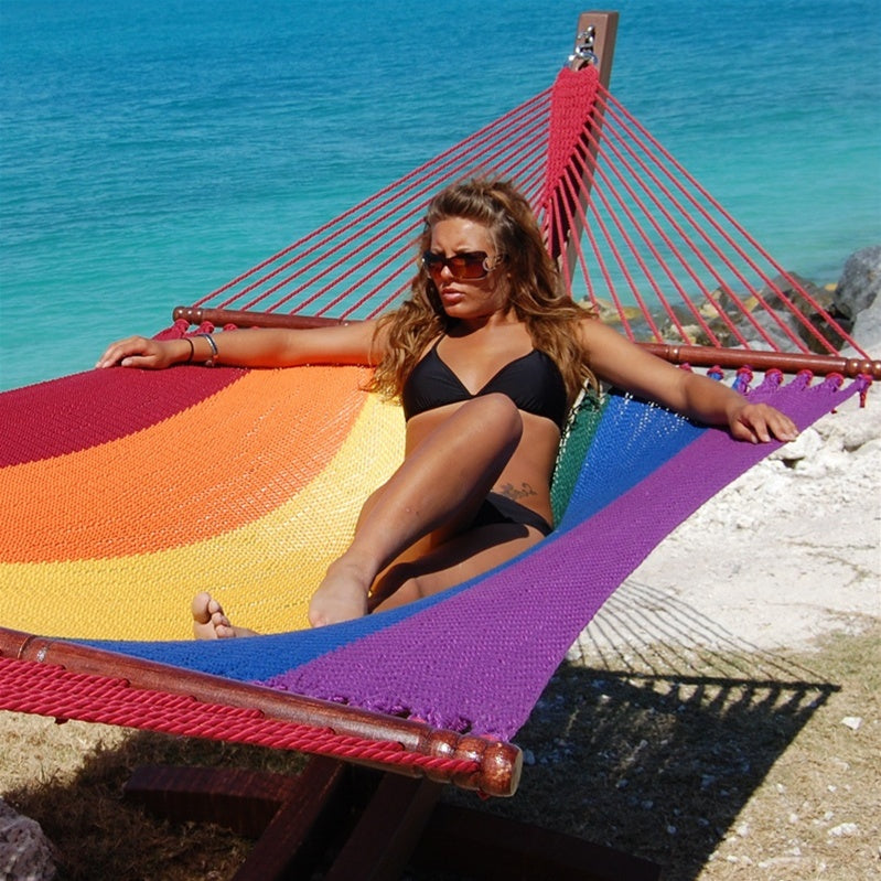Woman relaxing in the Rainbow Jumbo Caribbean Hammock on the Wood Arc Hammock Stand beside the ocean
