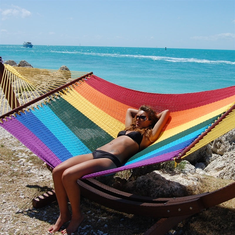 Woman relaxing in the Rainbow Jumbo Caribbean Hammock on the Wood Arc Hammock Stand beside the ocean