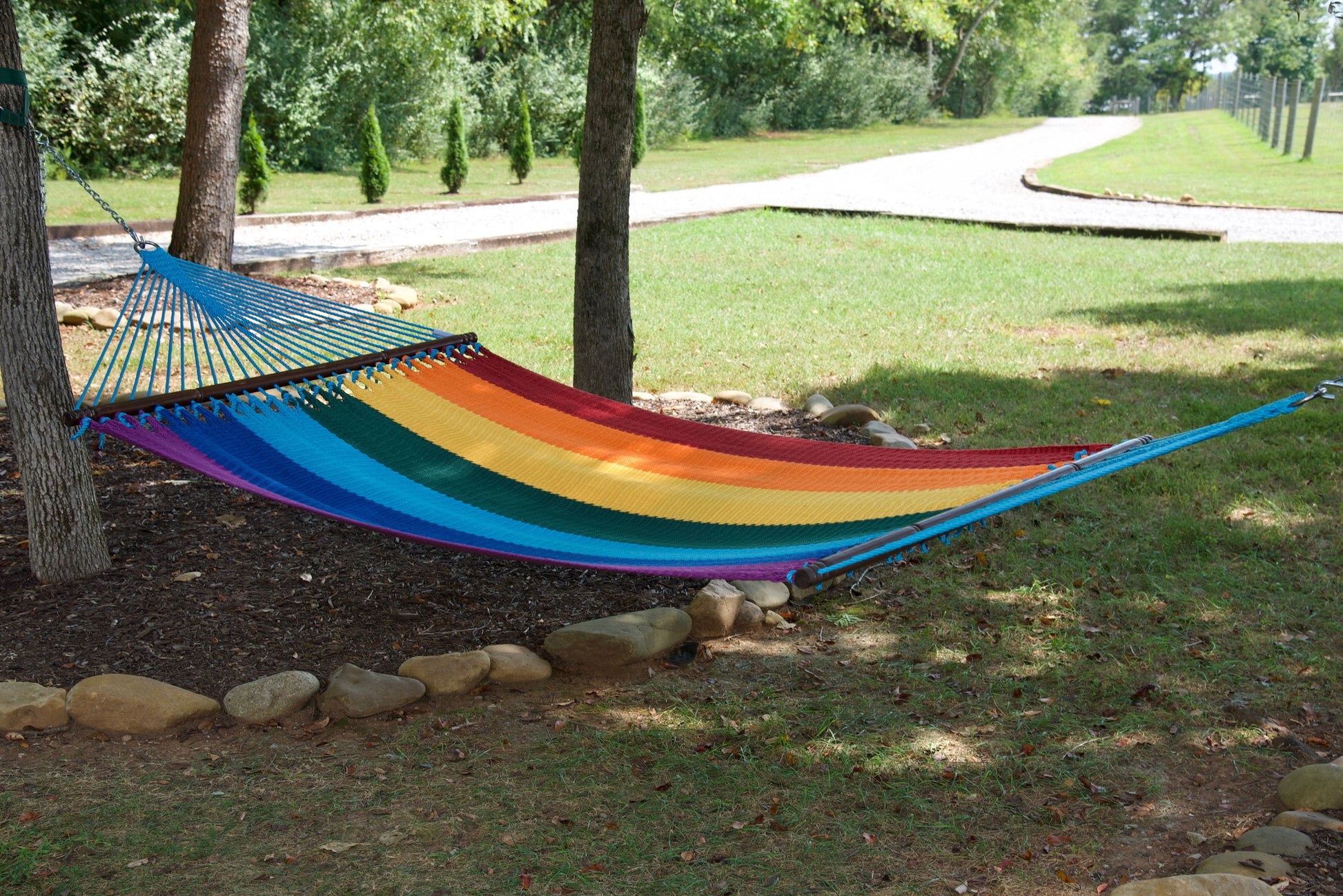 Rainbow Jumbo Caribbean Hammock hanging between two trees in a backyard