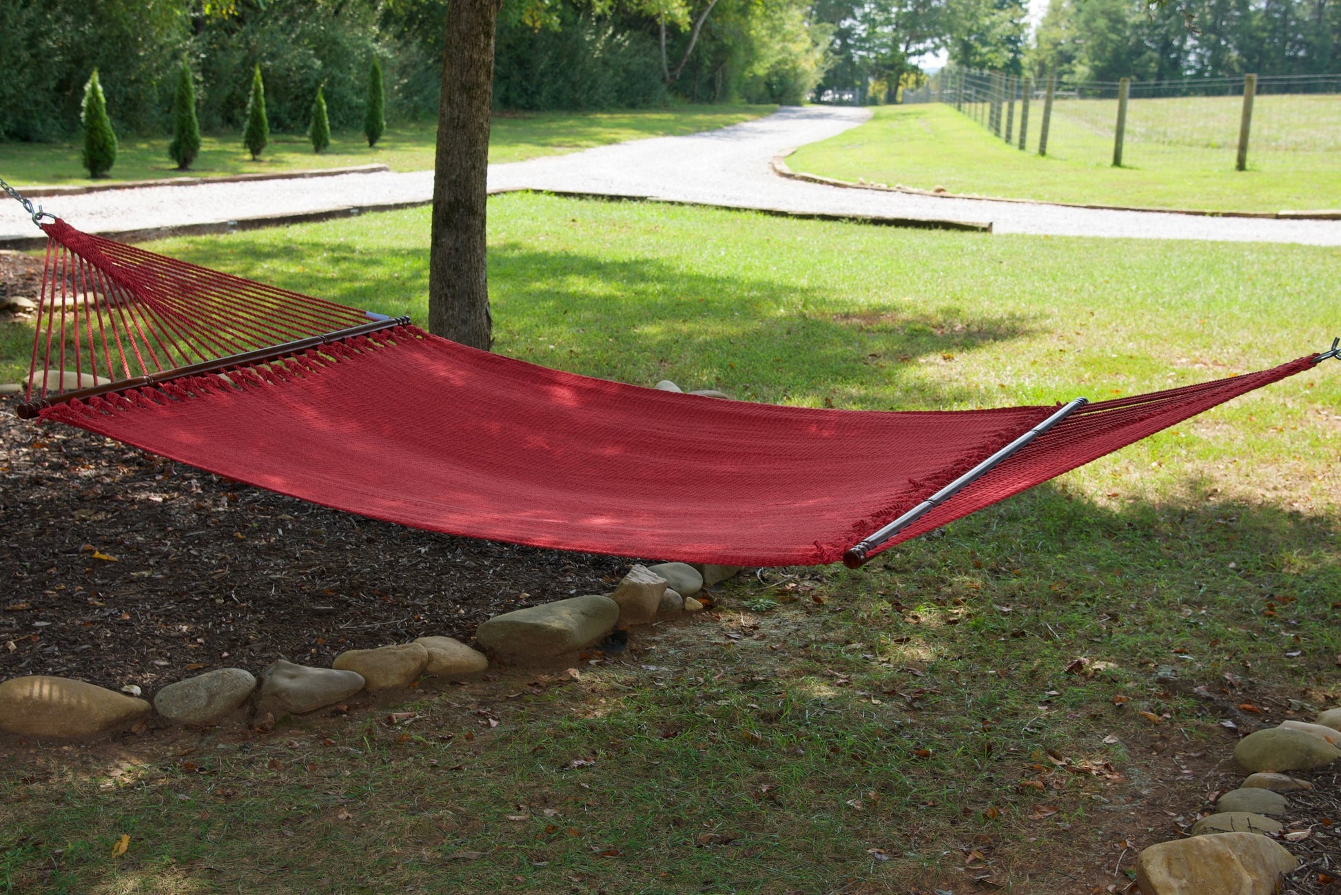 Red Jumbo Caribbean Hammock hanging between two trees in a backyard