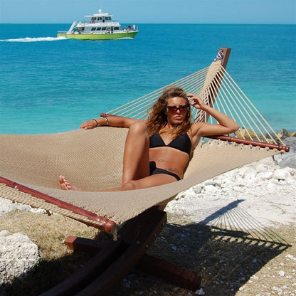 Woman relaxing in the Tan Jumbo Caribbean Hammock on the Wood Arc Hammock Stand beside the ocean