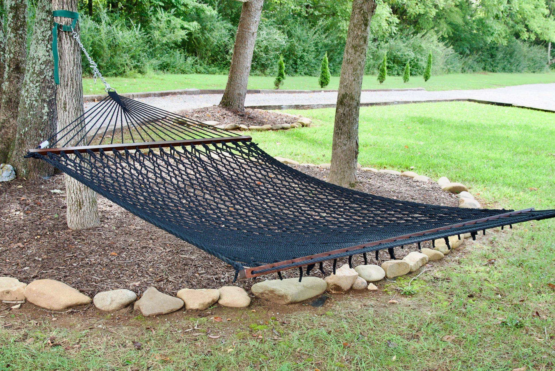 Black Jumbo Rope Hammock hanging between two trees in a landscaped backyard.
