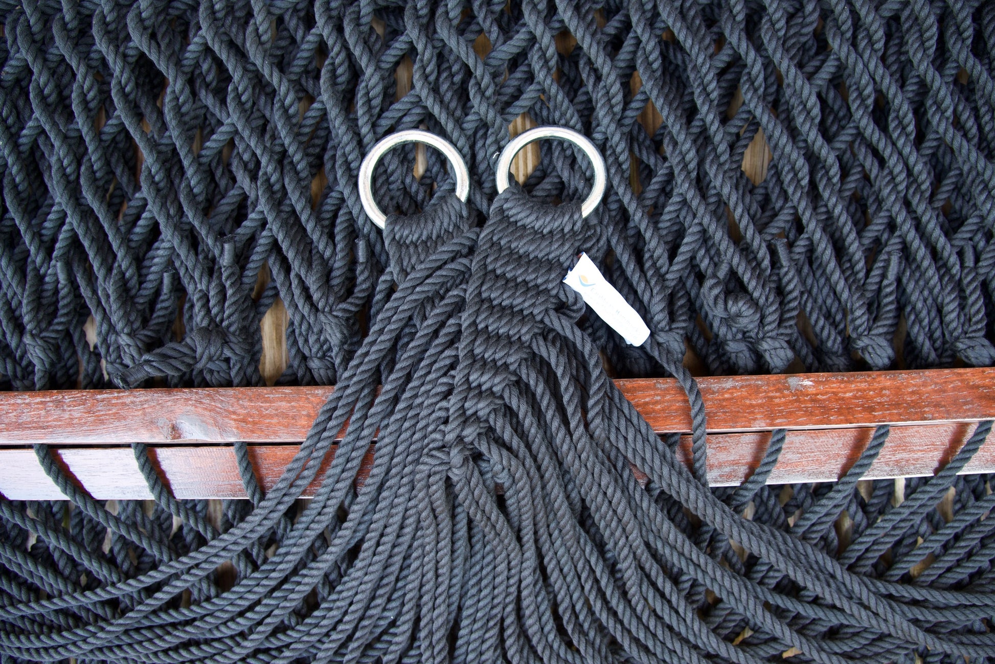 Close view of the gathered Black end cords and O-rings of the Jumbo Rope Hammock above the wood spreader bar.