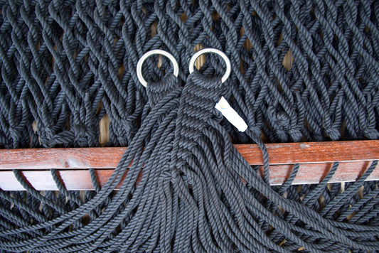 Close view of the gathered Black end cords and O-rings of the Jumbo Rope Hammock above the wood spreader bar.