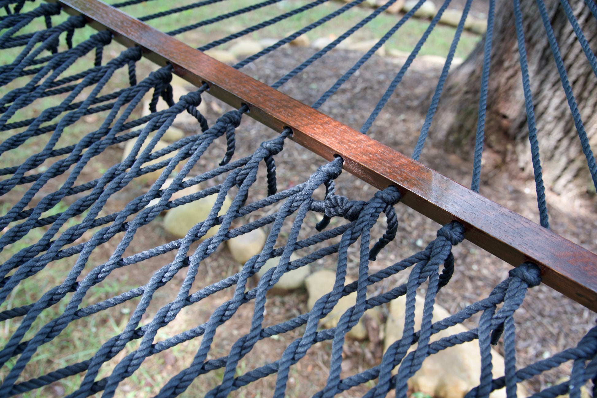 Close view of the Black end cords threaded through the wood spreader bar of the Jumbo Rope Hammock.