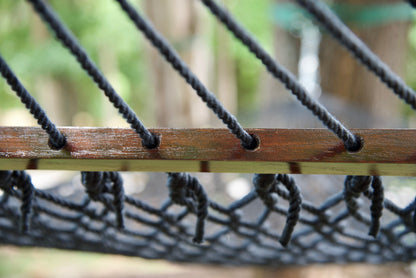 Close view of the Black end cords threaded through the wood spreader bar of the Jumbo Rope Hammock.