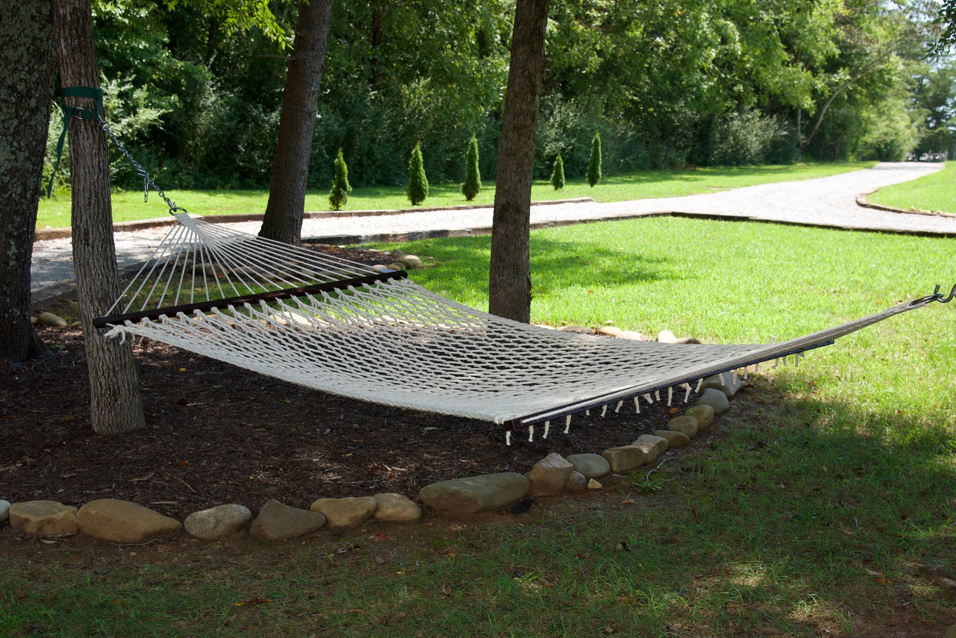 Cream Jumbo Rope Hammock hanging between two trees in a landscaped backyard.