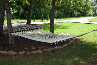 Cream Jumbo Rope Hammock hanging between two trees in a landscaped backyard.