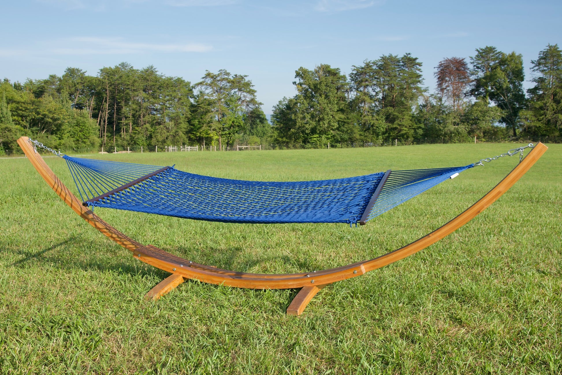 Dark Blue Jumbo Rope Hammock hanging on a Wood Arc Hammock Stand in an open grass field.