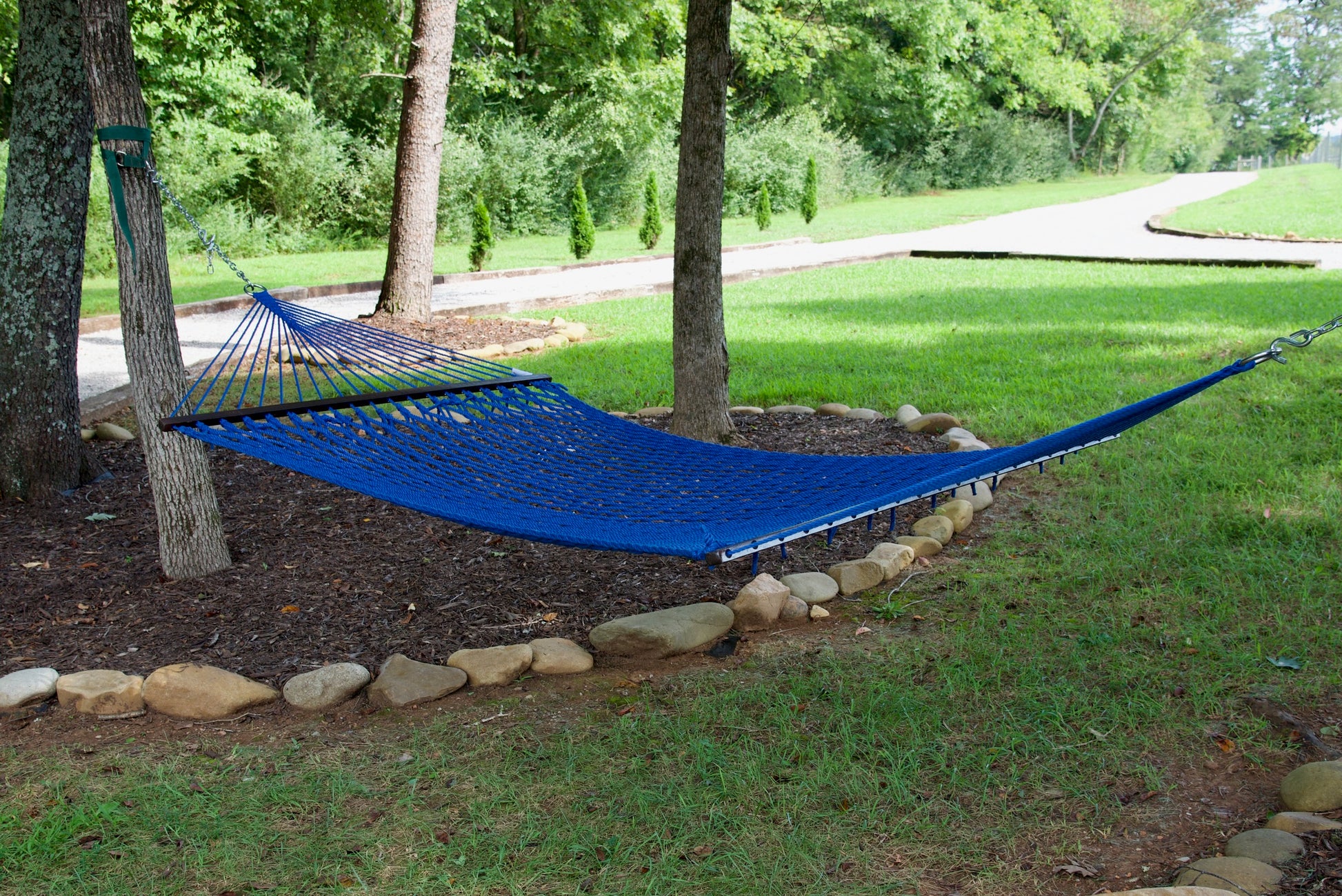 Dark Blue Jumbo Rope Hammock hanging between two trees in a landscaped backyard.