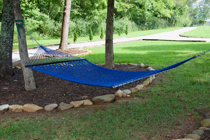 Dark Blue Jumbo Rope Hammock hanging between two trees in a landscaped backyard.
