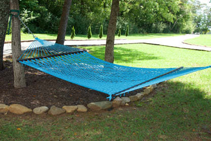 Light Blue Jumbo Rope Hammock hanging between two trees in a landscaped backyard.