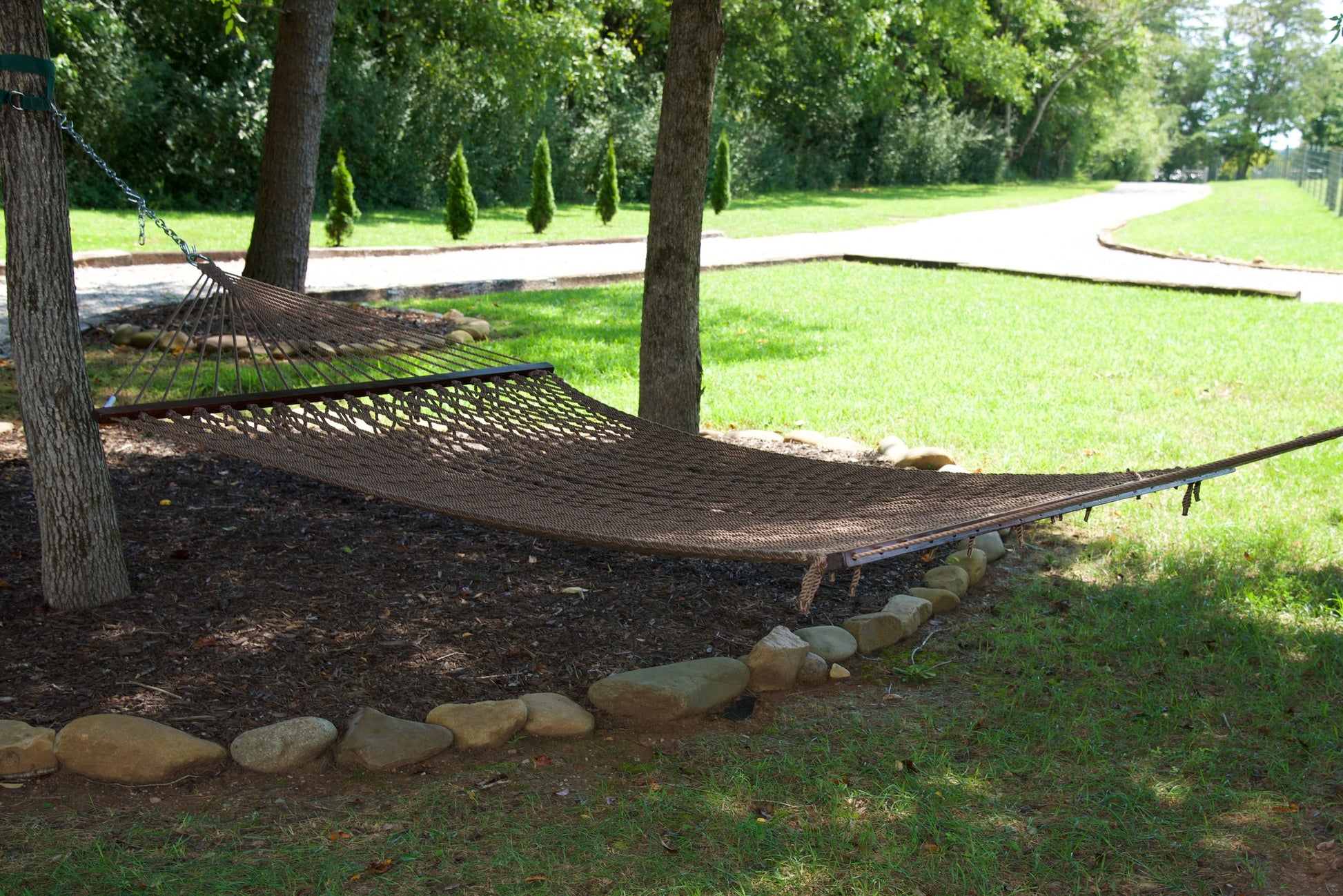 Mocha Jumbo Rope Hammock hanging between two trees in a landscaped backyard.