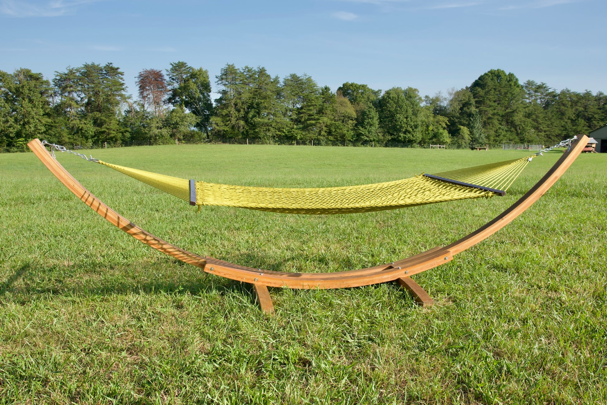 Olive Jumbo Rope Hammock hanging on a Wood Arc Hammock Stand in an open grass field.