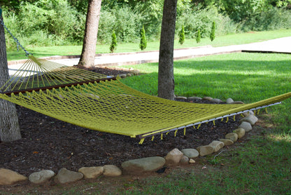 Olive Jumbo Rope Hammock hanging between two trees in a landscaped backyard.