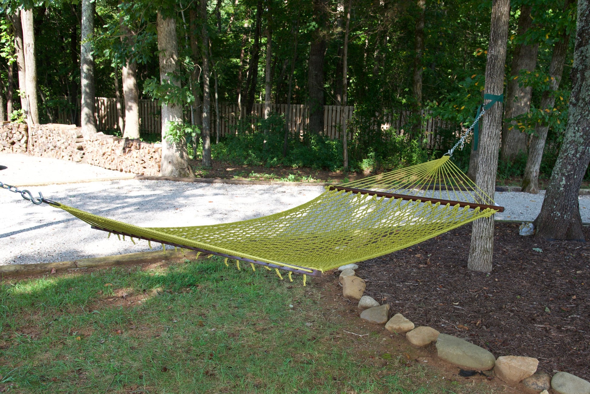 Olive Jumbo Rope Hammock hanging between two trees in a landscaped backyard.
