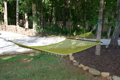 Olive Jumbo Rope Hammock hanging between two trees in a landscaped backyard.