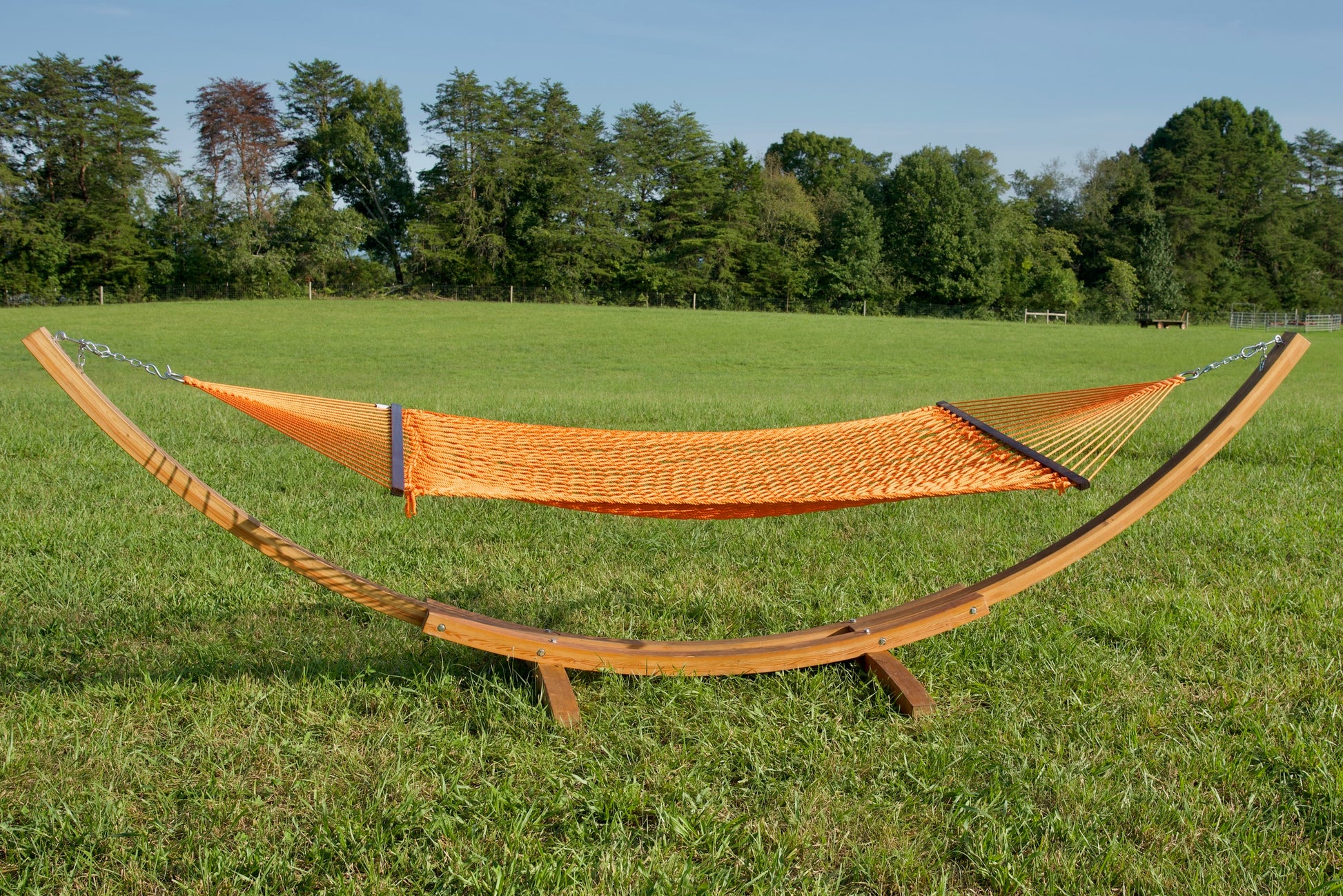 Orange Jumbo Rope Hammock hanging on a Wood Arc Hammock Stand in an open grass field.