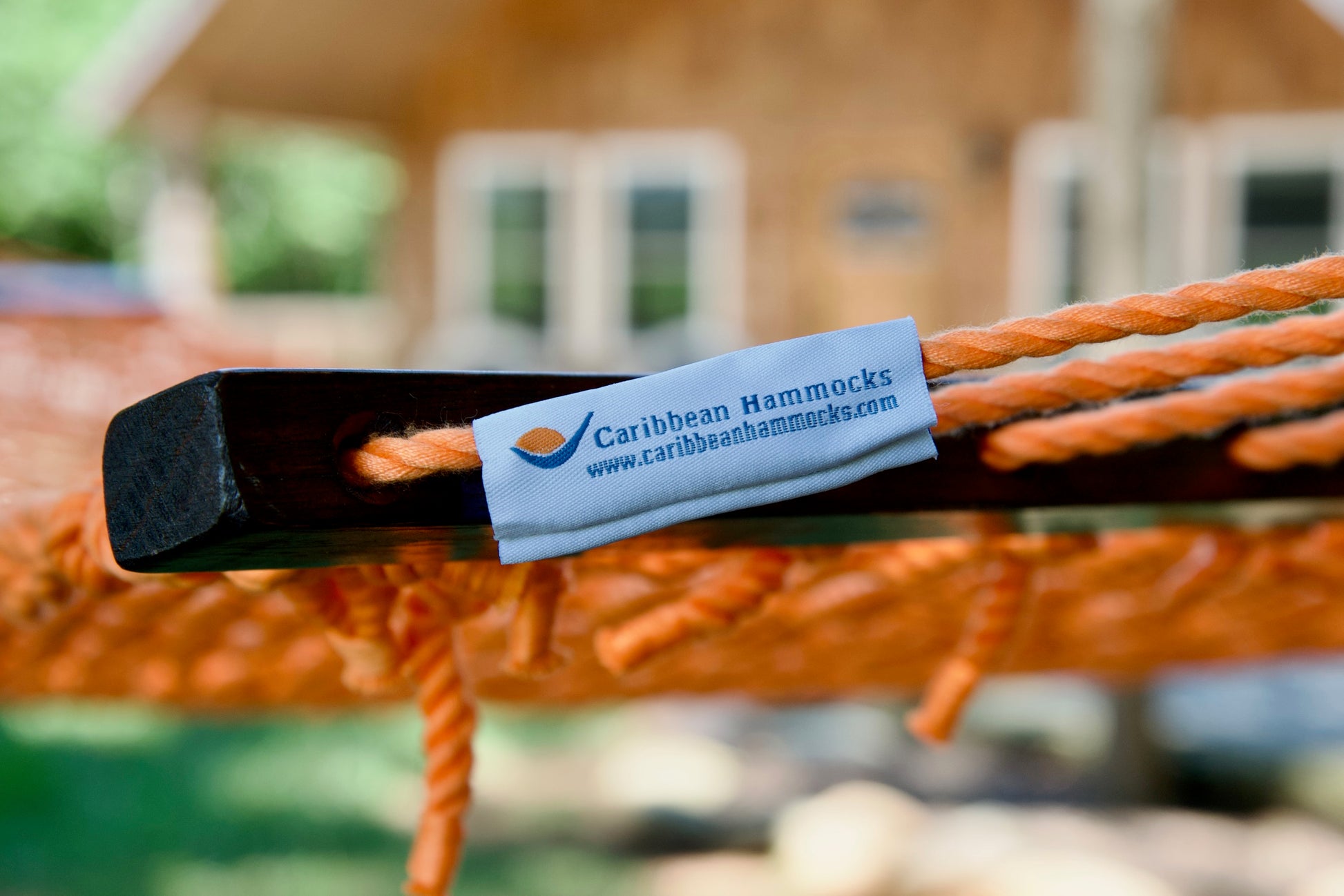 Caribbean Hammocks brand label on the wood spreader bar of the Orange Jumbo Rope Hammock.