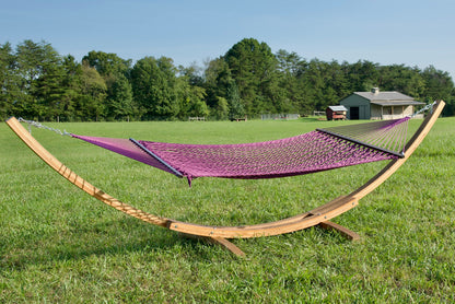Purple Jumbo Rope Hammock hanging on a Wood Arc Hammock Stand in an open grass field.