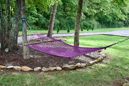 Purple Jumbo Rope Hammock hanging between two trees in a landscaped backyard.