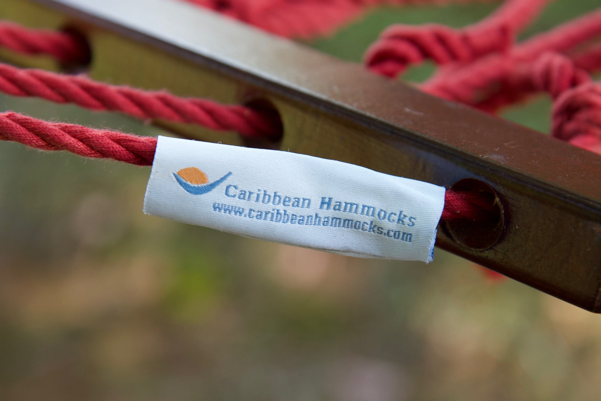 Caribbean Hammocks brand label on the wood spreader bar of the Red Jumbo Rope Hammock.